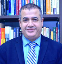A profile of a man with a tie (stripey) and suit infront of a book shelf